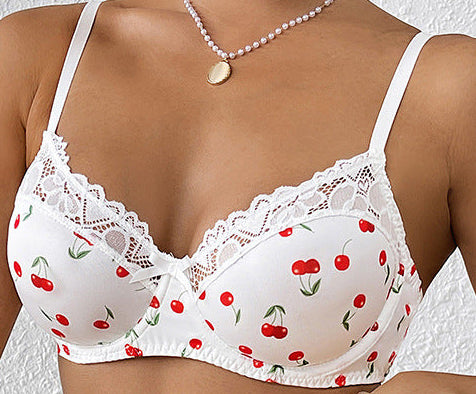 Woman wearing a white lace bralette with cherry pattern and blue jeans against a white background