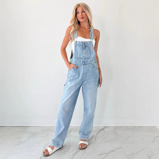 Woman wearing light blue denim overalls against a white background Women autumn tooling denim suspender pants in washed blue style