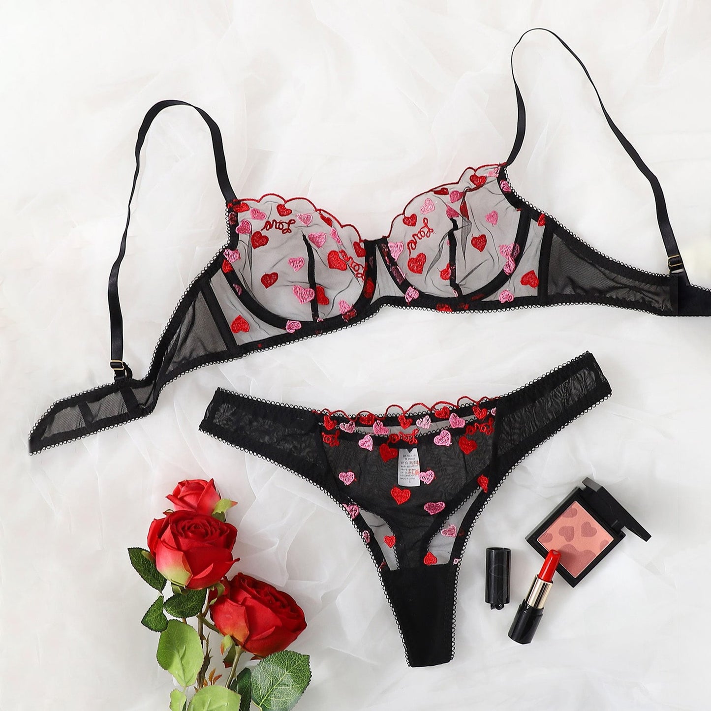 Black lingerie set with heart patterns on a white background, accompanied by red roses and makeup items.