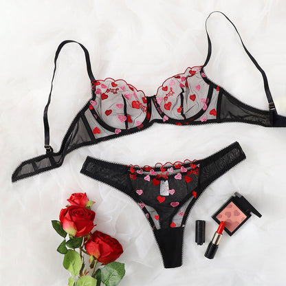 Black lingerie set with heart patterns on a white background, accompanied by red roses and makeup items.