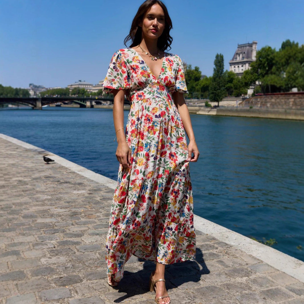 Woman in a floral dress standing by a river with a cityscape in the background