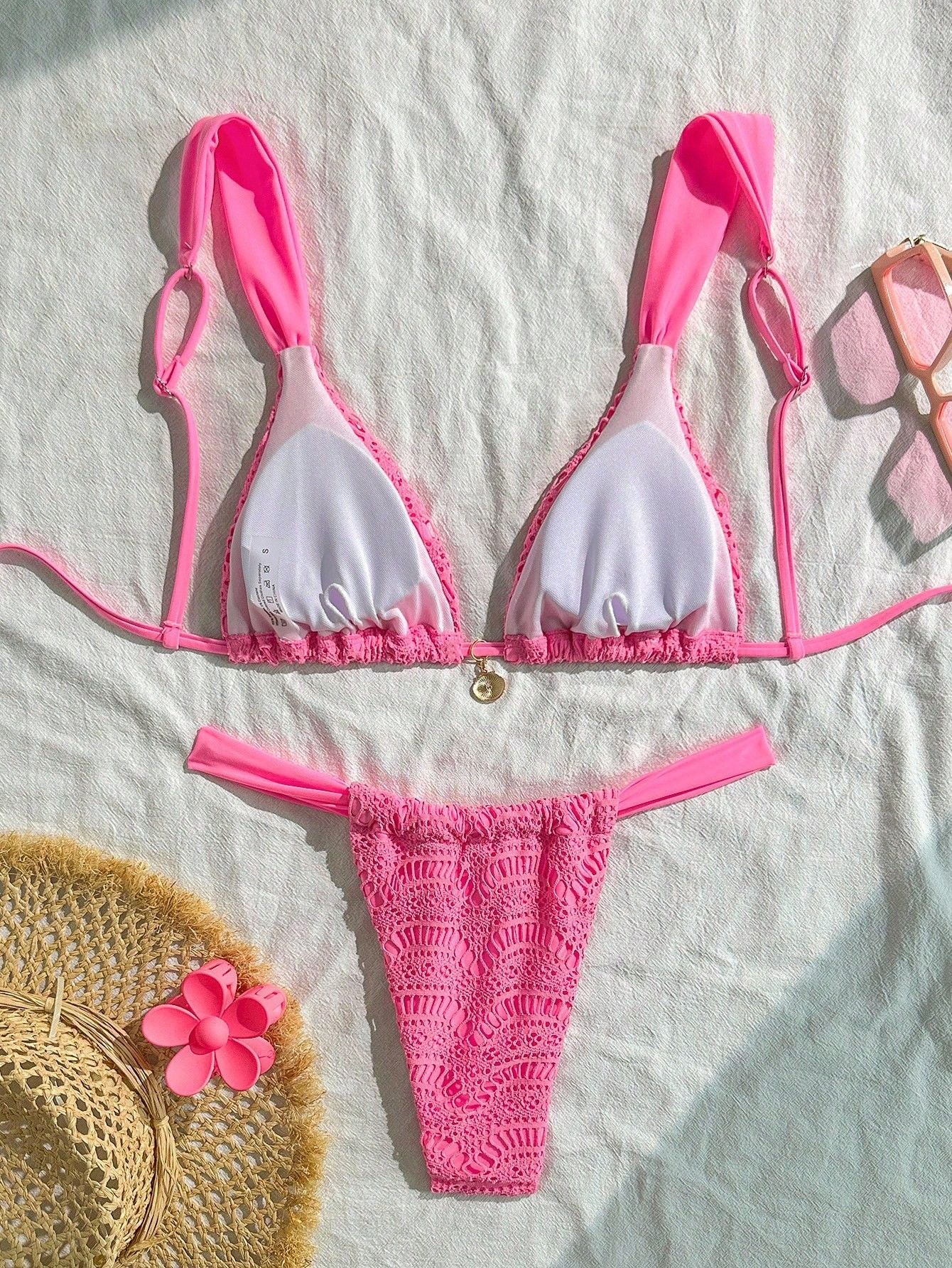Pink bikini set on a textured surface with a straw hat and flowers.