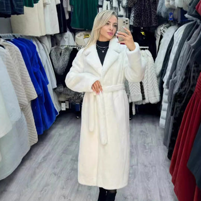 Woman taking a mirror selfie wearing a long white fur coat in a clothing store.