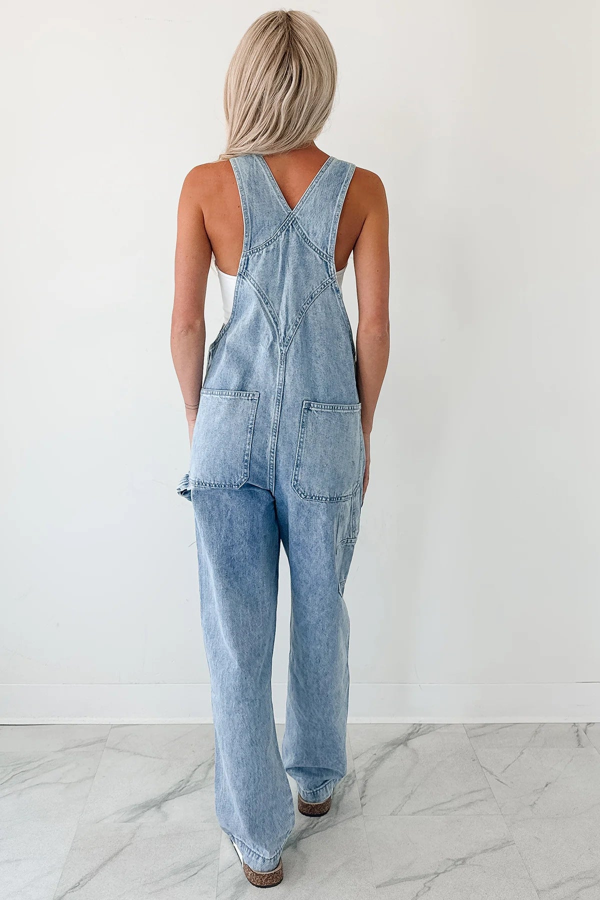 Person wearing light blue denim overalls on a white background Women autumn tooling denim suspender pants in washed blue style