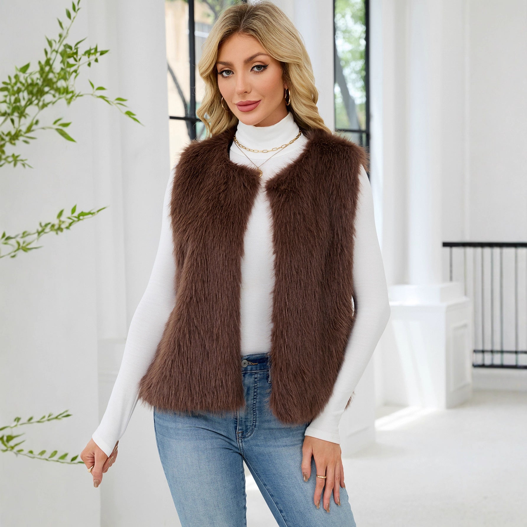 Woman wearing a brown fur vest over a white turtleneck and blue jeans indoors.