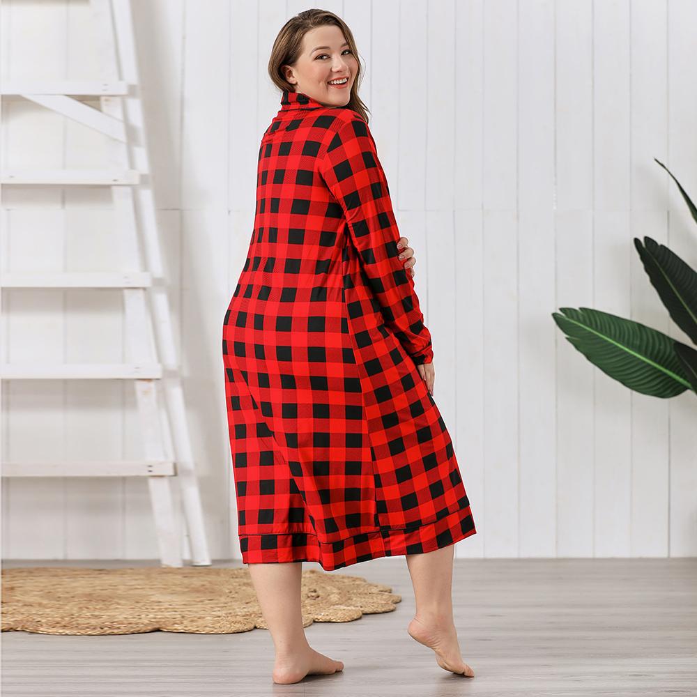 Woman wearing a red and black checkered dress standing in a room with white walls and a plant.