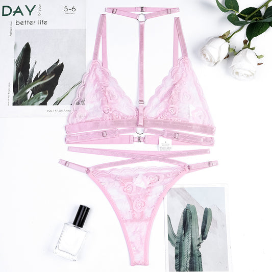 Pink lingerie set with floral lace details on a white background with plants.