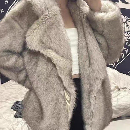 Gray fur coat worn by a person on a bed with a patterned blanket.